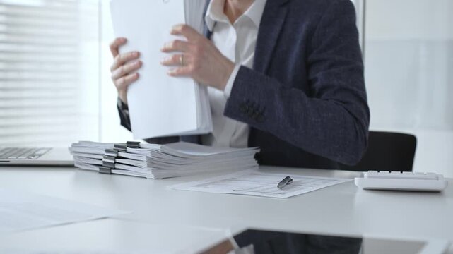 Business professional sorting a large stack of financial reports and tax forms with binder clips on a busy office desk. Audit and taxes