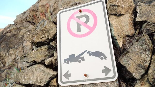 No parking sign with tow away symbol on a rock wall.