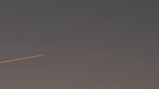 Airplane leaving a glowing contrail across twilight sky