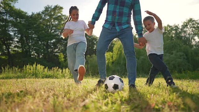 The children, a boy and a girl, are playing soccer with a man who is probably their father. The boy tries to kick the football while the girl laughs. It a joyful game between father and children.