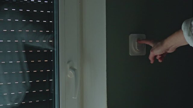Female hand using switch to lift outdoor roller shutter indoors. Concept of light regulation and protection