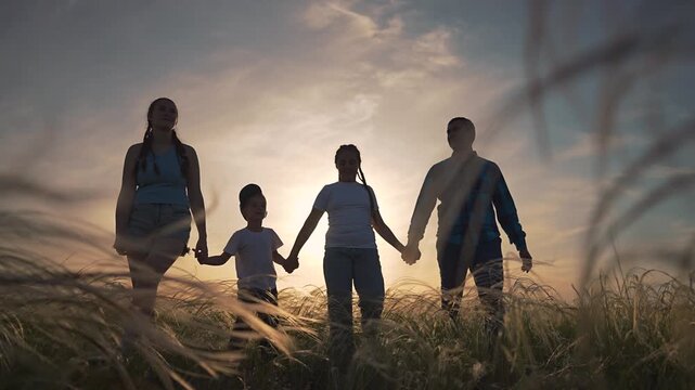 Parents holding hands children walking through grass. Family walking in sunset light. Father walks beside son. Mother and daughter walking. Holding hands shows unity. Happy walking kids and parents