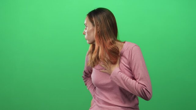 Woman redhead young gasping with hand on chest looking sideways wearing pink sweater in studio; anxiety breathlessness concern.