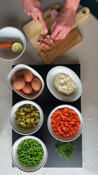Hands cutting sausages for traditional Olivier Ruska Salad on Chopping Board