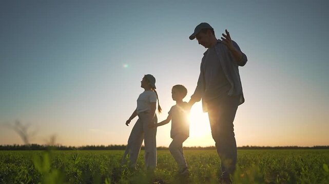 Father daughter son walking field sunset. Family silhouette holding hands together moving forward. Field walk father daughter son close. Father gently holding daughter son while walking field together