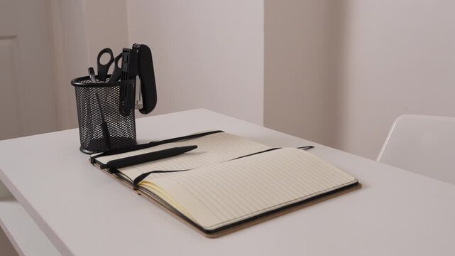 Profile side view of workspace with notebook, stapler and scissors, minimal office desk setup, clean and modern business environment.
