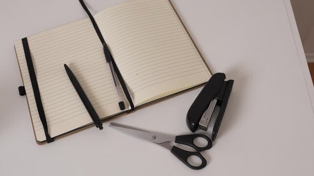 Top view workspace with notebook, pen, scissors and stapler on desk, flat lay composition, minimal office and study concept with copy space.
