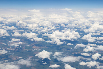 Fototapeta premium View from an airplane of the earth under fluffy white clouds with a blue sky as a textured background