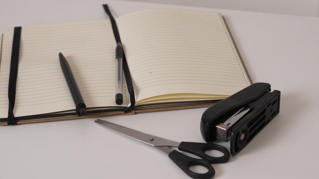 Open blank notebook with pen, scissors and stapler on desk, workspace concept for planning, writing and office organization, clean minimal style.
