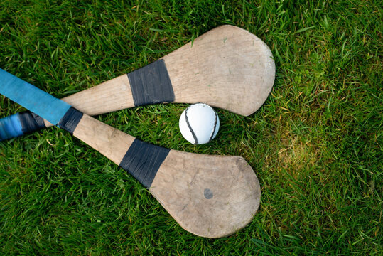 Two wooden hurleys and white sliotar lying on green grass evoke traditional Irish hurling, outdoor team sport, summer play and athletic heritage