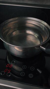 Close-up of electric induction cooktop glowing red as pot with water is placed on it, modern kitchen cooking process, heating concept, home lifestyle scene
