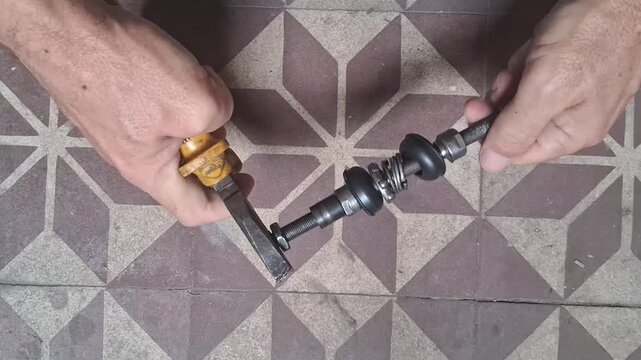 Hands assembling intricate mechanical parts onto a threaded metal rod with a specialized tool, video.
