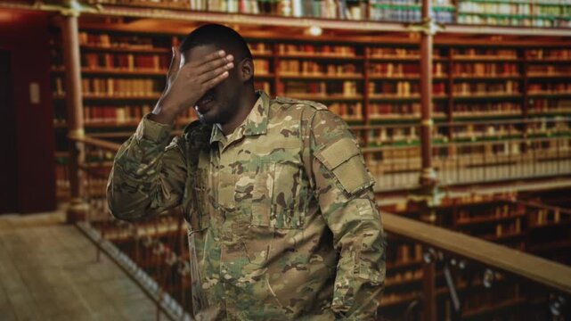 Man soldier in camouflage uniform covers his face with hand beside tall bookshelves on a balcony in a building; stress reflection.