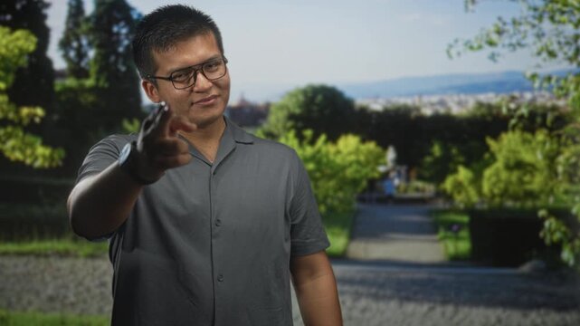 Man points finger at camera in a sunny park near a tree lined walkway wearing glasses and gray shirt; confidence connection.