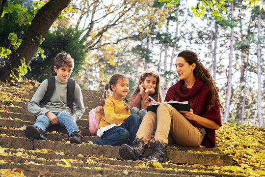 Energetic teacher leads a small, diverse group of preschoolers on an outdoor nature exploration, pointing out interesting details of the local flora and fauna.
