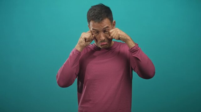 Man with moustache rubbing eyes with hands and pouting mouth wearing maroon longsleeve shirt in studio; mock sadness.