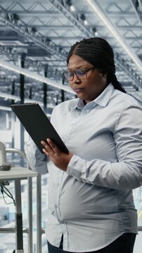 Vertical video Reviewing schematics, semiconductors and portrait of smiling woman in smart factory. Overseeing layouts, EDA software and cheerful african american businesswoman in industry 4.0 plant
