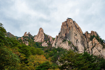 Fototapeta premium Majestic granite peaks of Seoraksan Mountain with autumn foliage under a cloudy sky, South Korea.