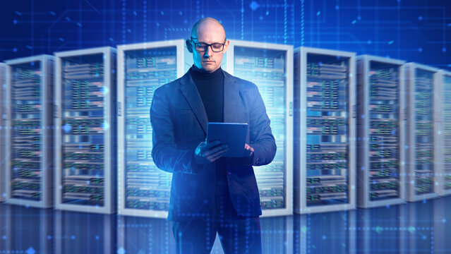 Data center, IT infrastructure. System administrator monitors server racks and network equipment on a tablet in a high-tech server room.