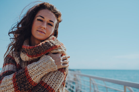 Brunette woman in sweater hugging herself and smiling on pier