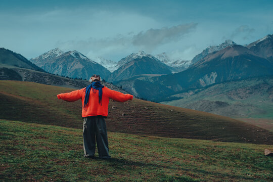 Redhead athletic woman in bright warm clothes looking up with arms open in mountains