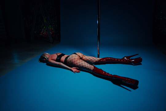 Tired woman lying on studio floor in red boots, pole dance concept