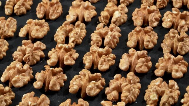 High-angle rotating texture of shelled walnut kernels neatly arranged in diagonal rows on a black background. Premium organic food geometry concept.