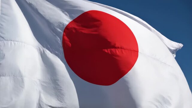 Close-up of the Japanese national flag (hinomaru) waving in breeze, emphasizing the vivid red circle on white fabric with folds, stitching, shadows and blue sky backdrop