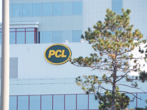 Ottawa, Ontario, Canada &ndash; July 26, 2025: The yellow and green "PCL Construction" logo is mounted on a white office building partially obscured by a tree on Riverside Rd.
