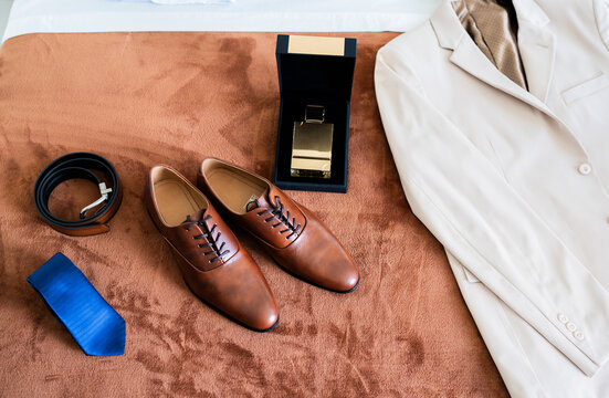 Elegante conjunto de traje de novio con accesorios y perfume sobre cama en preparaci&oacute;n para boda