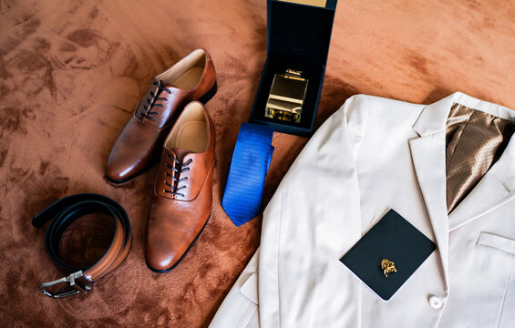 Preparaci&oacute;n elegante del novio con traje beige, zapatos de cuero y accesorios sobre cama antes de la boda