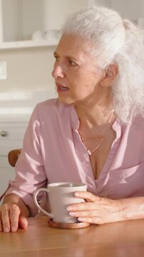 Senior woman holding mug, turning to voice, reacting as animated health icons appearing beside her