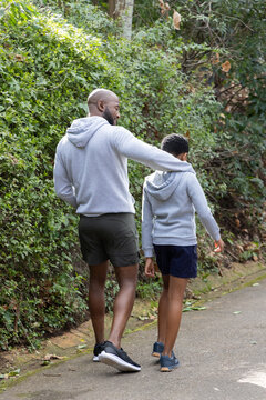 African American father and son walking together on paved park path wearing matching gray hoodies