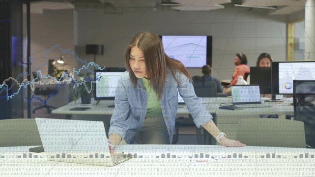 Receiving chart update, woman leaning over laptop noting while checking wall charts to review data