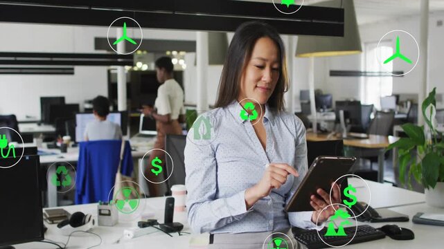 Tapping tablet, mid-adult Korean woman wearing blue blouse scrolling at open office, with AR icons