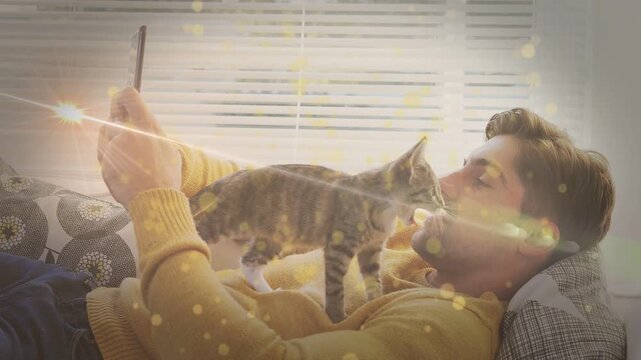 Man reclining holding phone, kitten leaping onto chest seeking pet sparking tech flares across face