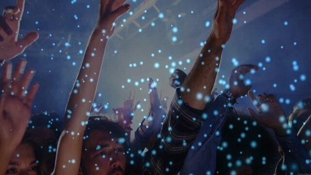 Crowd raising arms at concert cheering while stage light rising and blue confetti drifting on faces