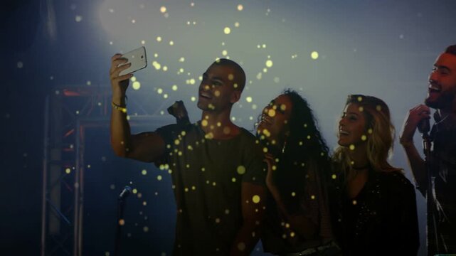 Vertical video: Man raising phone, group posing for selfie on music stage amid confetti, checking