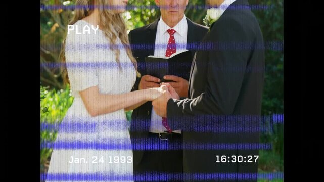 Officiant reading cuing groom placing wedding ring under arch while timestamp PLAY glitching frames