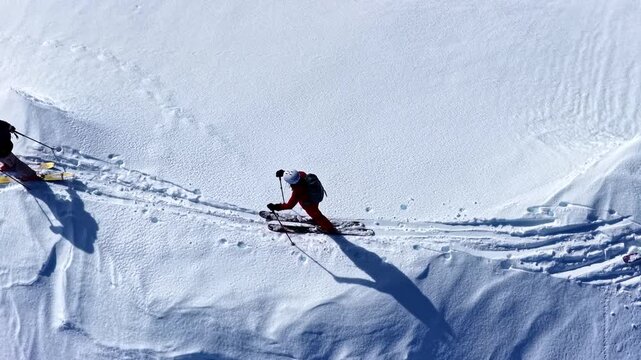 Cinematic rising above two skiers skinning uphill along a narrow snowy ridge in Nauders Austria with long shadows on textured winter snow - top down aerial slow motion shot
