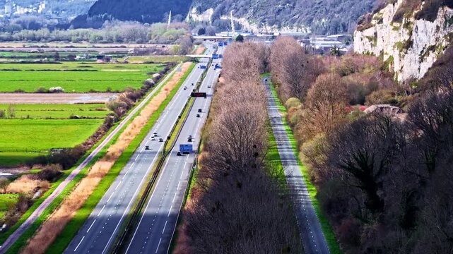 Aerial drone shot reveals multi-lane French autoroute cutting through scenic valley flanked by white chalk cliffs and green farmland near Le Havre in Normandy, France