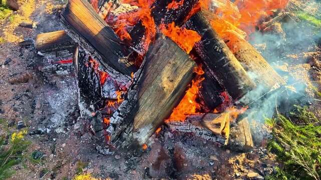 Revealing shot moves across pile of heavy timber logs engulfed in orange fire and white smoke during cold winter evening