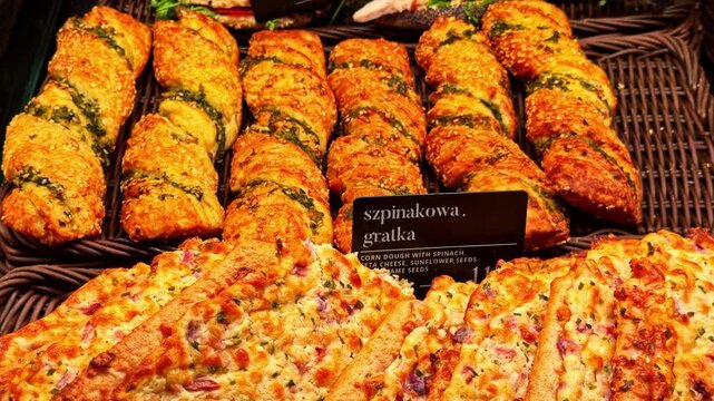 Freshly baked savory pastries with spinach, cheese, and seeds on display for sale in a local bakery showcase. Close-up