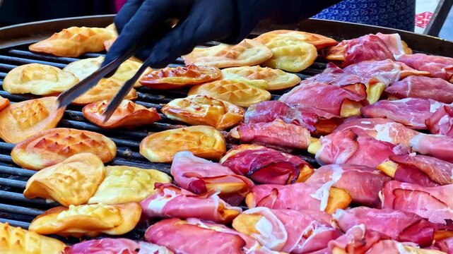 Chef grilling traditional polish oscypek cheese, some wrapped in bacon, at a street food stall in Krakow, Poland
