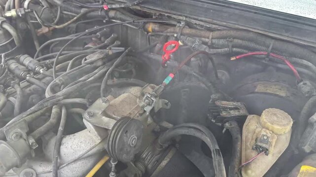 Zoomed view of a smoking car engine with visible wires and pipes
