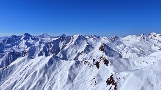 Snow covered alpine mountain range with sharp peaks under clear blue sky in Serfaus Fiss Ladis Austria, aerial panoramic backdrop flyover people