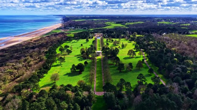 Normandy American Cemetery landscape with rows of graves beside coastline and forest in Normandy France, aerial, centered static time lapse