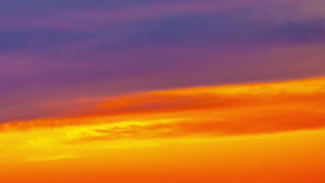 Aerial close-up of dramatic layered sunset sky transitioning from deep purple through fiery orange and red to brilliant golden yellow with airplane passing through