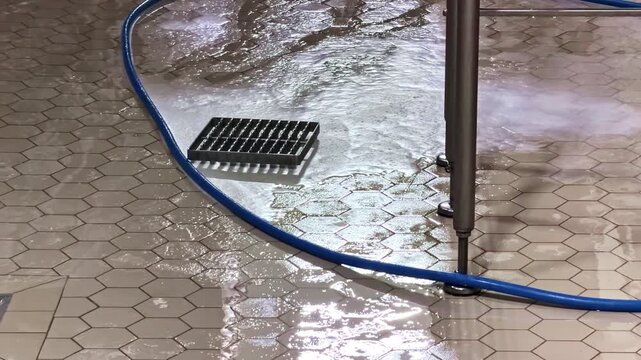 Water hose cleaning tile floor, industrial setting, blue pipe
