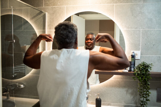Senior man flexing muscles in home bathroom mirror
